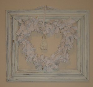the frame for the heart-shaped wreath came from the base of a stripped lampshade. Strips of torn white cotton were knotted onto that, and a white silk tassle that I bought at a sidewalk sale for $1.75 finishes it off