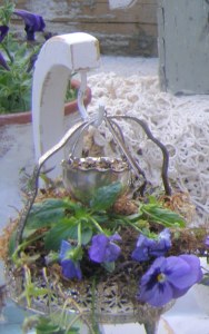 old faithful banana hanger with an antique silver plated condiment trivet planted with leggy pansies and a young ivy.